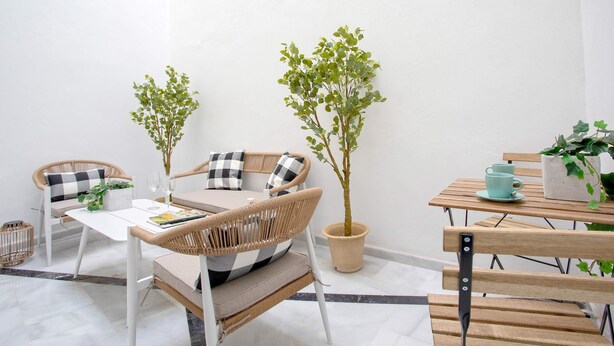 Un espacio al aire libre acogedor con muebles de mimbre, una mesita y dos macetas.