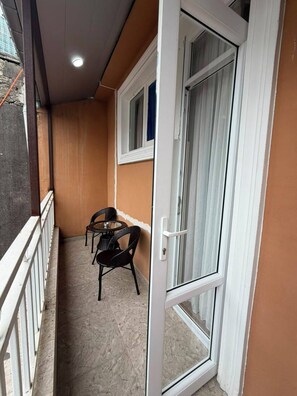 Un balcón con una puerta blanca, una mesa pequeña y dos sillas.
