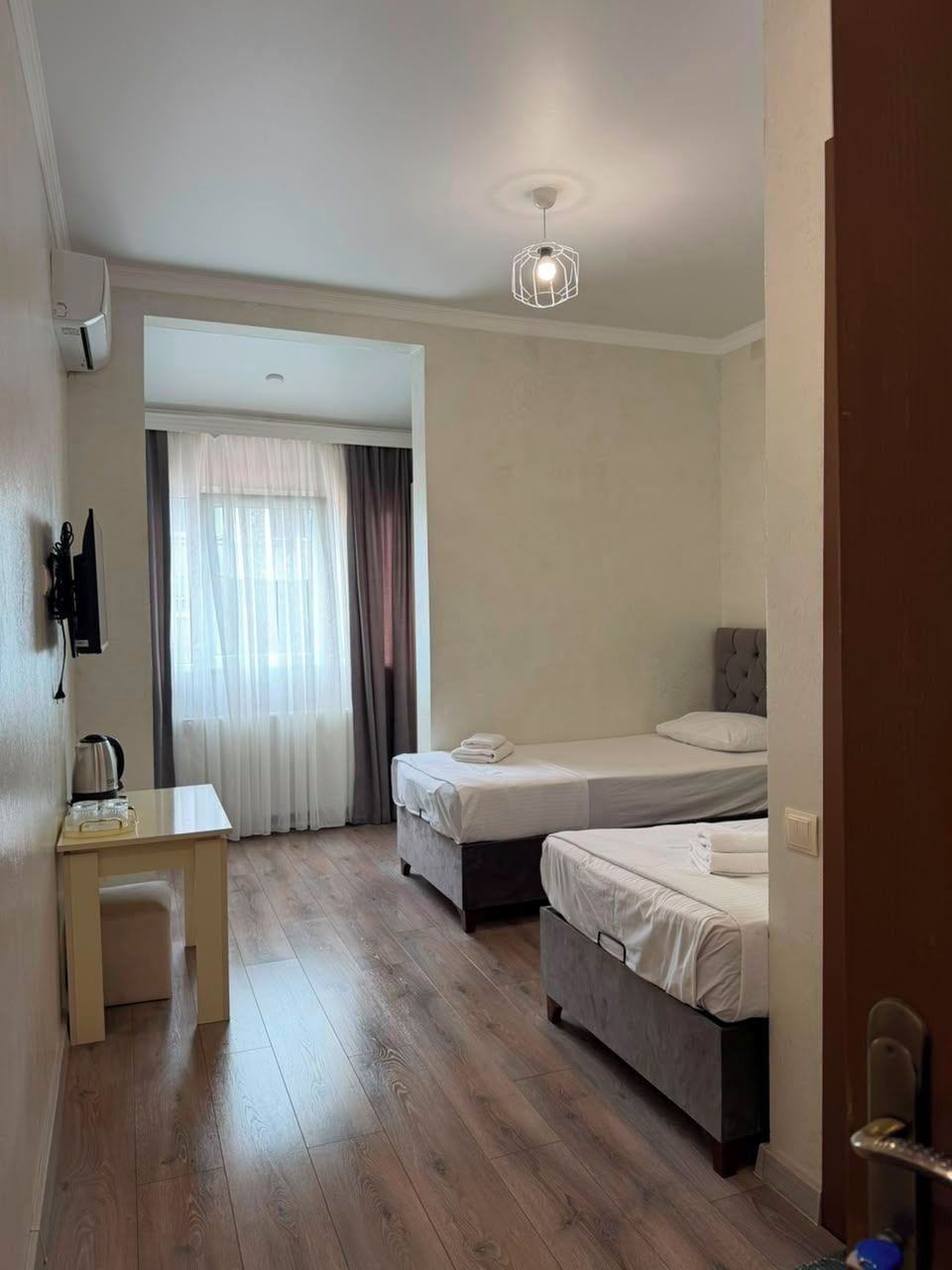 A hotel room with two beds, a desk, a chair, a wardrobe, and a bathroom door.