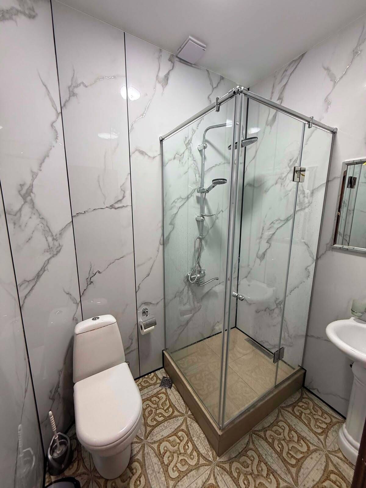 A bathroom with a glass-enclosed shower, a toilet, and a sink.
