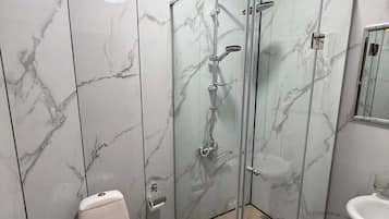 A bathroom with a glass-enclosed shower, a toilet, and a sink.