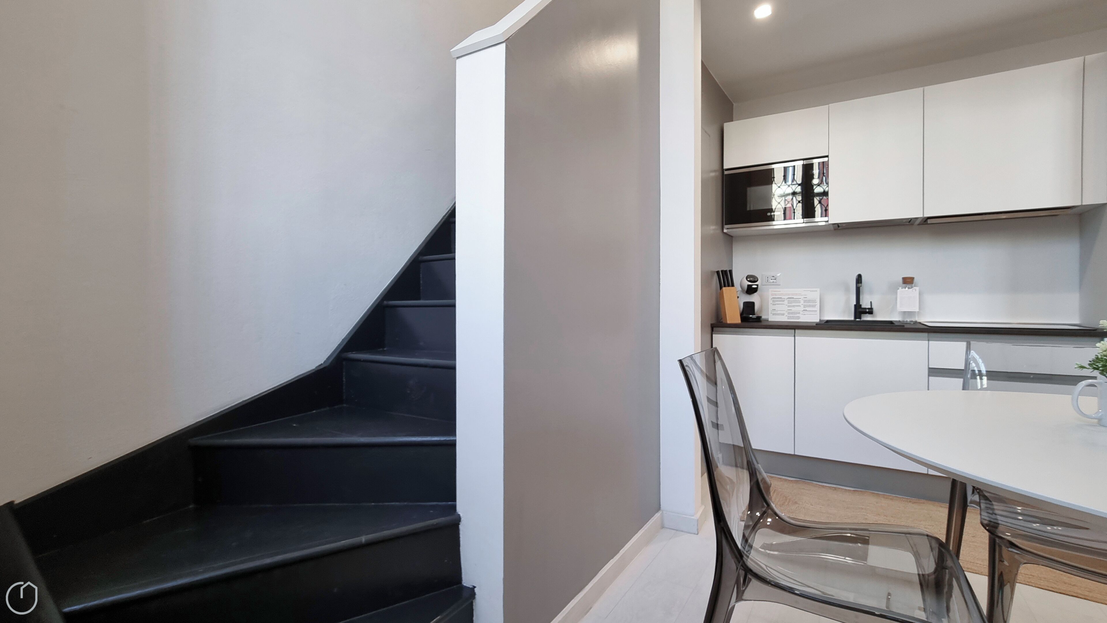 A modern kitchen with white cabinets, a black staircase, and a dining area with a round table and chairs.