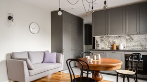 A modern kitchen with grey cabinets, a marble countertop, and a dining area with a round wooden table and black chairs. - RentPlanet - Apartament Rydygiera (Wroclaw)