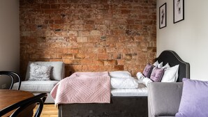 A room with a brick wall, a bed with pillows, a sofa, and a dining table. - RentPlanet - Apartament Rydygiera (Wroclaw)