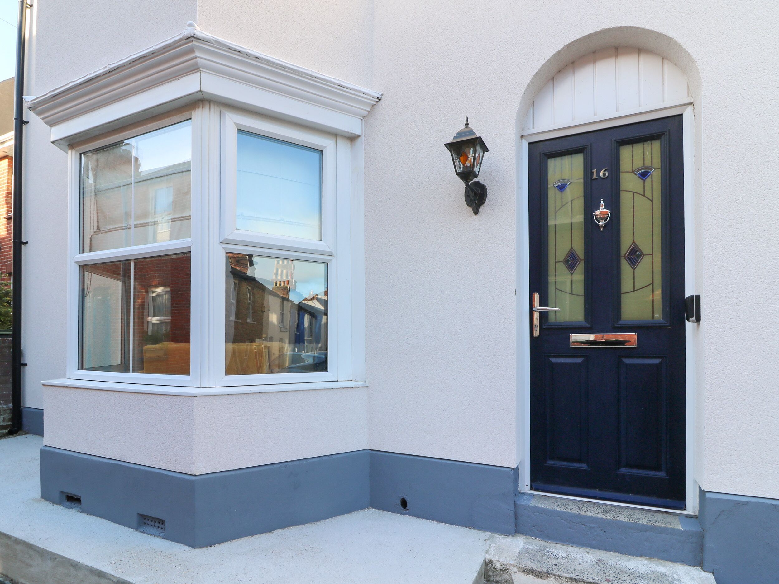 A house with a bay window and a dark front door with a number plate.