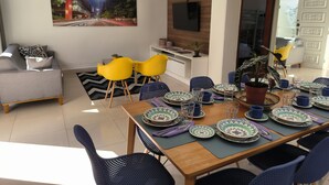 A modern living room with a dining area, featuring a large flat-screen TV, a sofa, and a dining table set with plates and glasses.