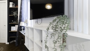 A room with a white built-in TV on a wall, a white shelf below it, and a hanging plant. - Italianway - Morosini 14 (Milan)