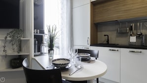 A modern kitchen with white cabinets, a black countertop, and a dining table set with a bowl, glasses, and a spoon. - Italianway - Morosini 14 (Milan)