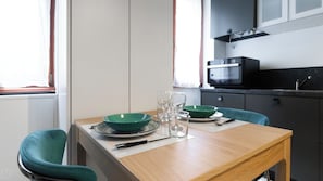 A dining area with a wooden table set for two, two green bowls, two wine glasses, and a knife.
