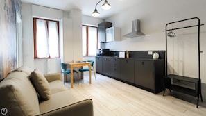 A compact living space with a sofa, a dining table with chairs, a kitchenette, and a clothes drying rack. - Italianway - Tartaglia 19 (Milan)
