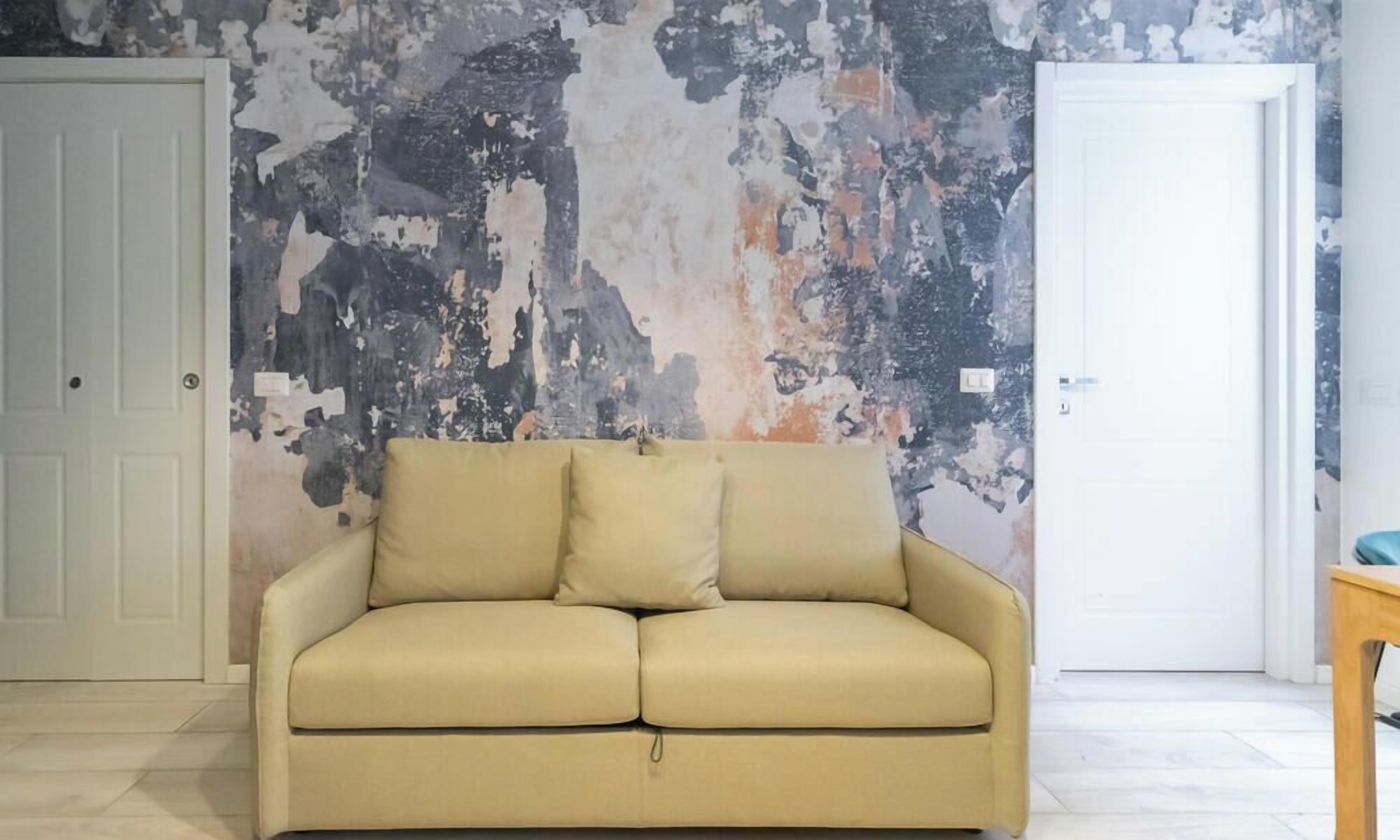 Una habitación con un sofá color beige, una puerta blanca y una pared con pintura descascarada.