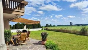 Un patio con pavimento in pietra, un tavolo di legno e sedie, con vista su un prato e un campo in lontananza.