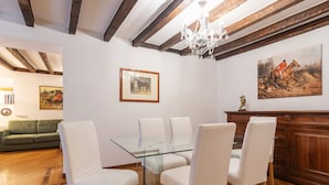 A dining area with a glass-top table and white chairs, wooden beams on the ceiling, and a chandelier. - easyhomes - Annunciata (Milan)