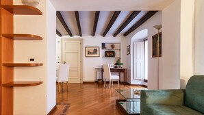 A modern living room with wooden floors, a green sofa, a glass coffee table, and a dining area with a white chair and a small table. - easyhomes - Annunciata (Milan)