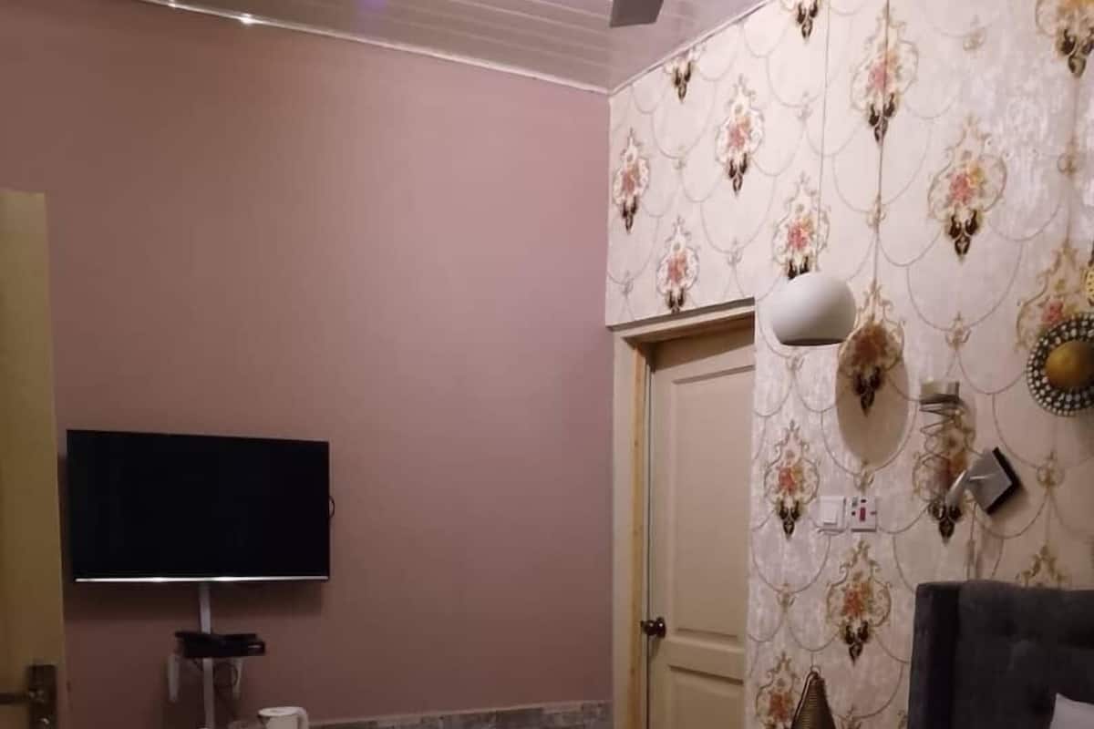 Ein Schlafzimmer mit einem Bett, einem an der Wand befestigten Fernseher, einer Tür und einer dekorativen Wandverkleidung.