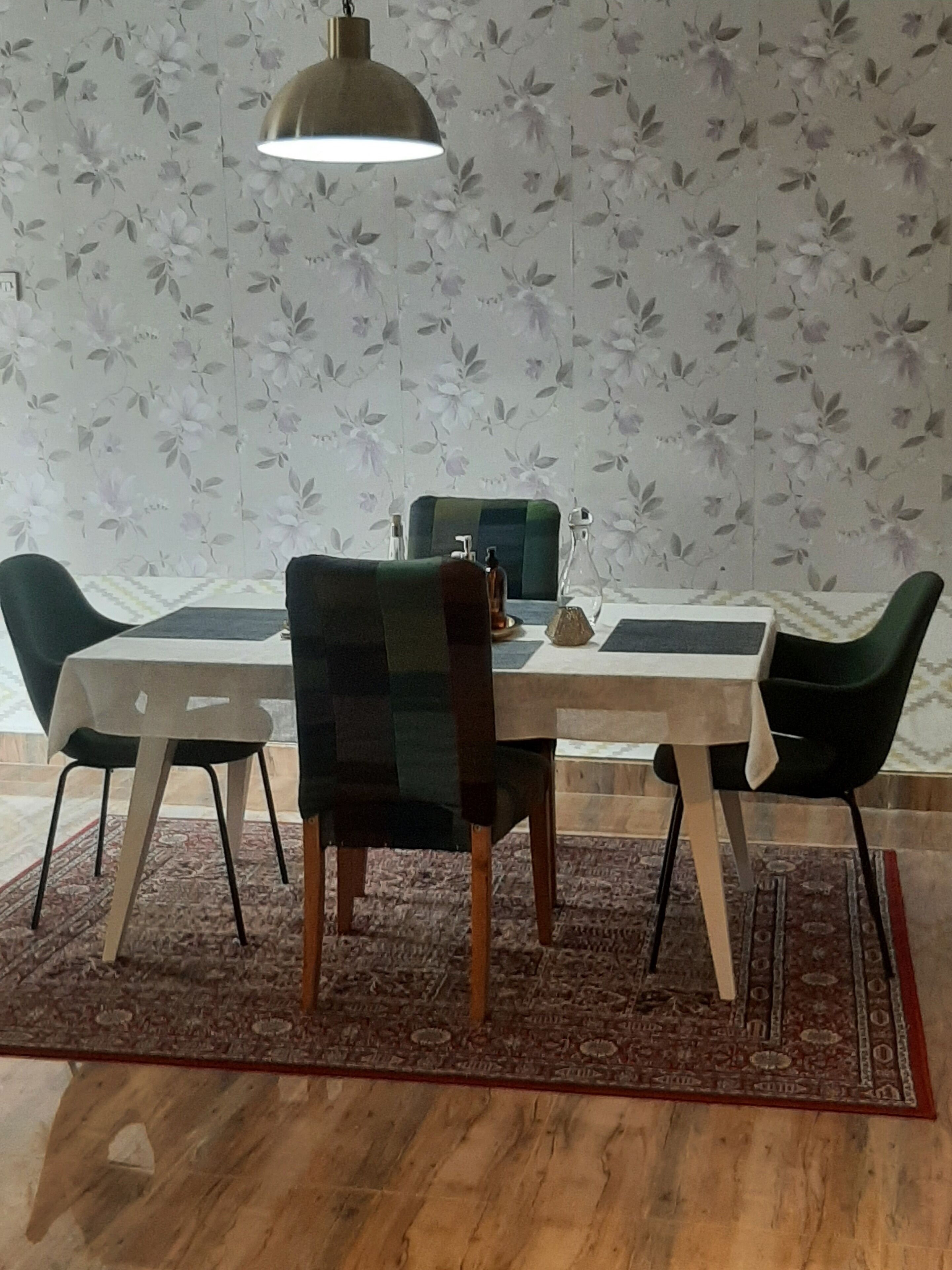 A dining area with a table and chairs, a hanging light fixture, and a floral wallpaper background.