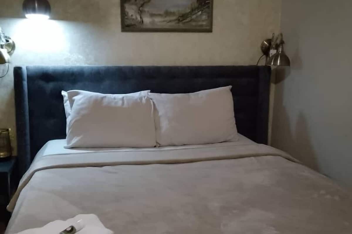 Ein ordentlich bezogenes Bett mit weißen Leinen, ein gefaltetes Handtuch und ein Landschaftsbild an der Wand.