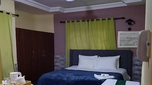 A hotel room with a bed, a small table with a tray of items, a chair, and a ceiling fan. - Nana Adu's Guesthouse (Koforidua)