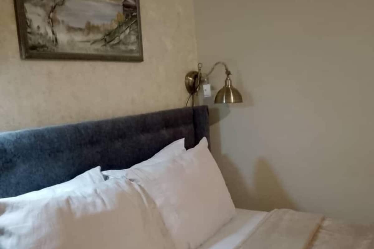 Ein ordentlich bezogenes Bett mit weißen Leinen und einem dunklen Kopfteil. Über dem Bett hängt ein gerahmtes Landschaftsbild.