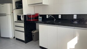 Une cuisine moderne avec des meubles blancs, un plan de travail noir, un four à micro-ondes encastré et un évier en acier inoxydable.