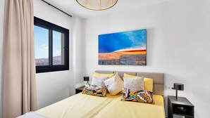 A modern bedroom with a large bed, a cityscape painting, and a view through a window. - Luxery 4 persons apartment pool side (Las Lagunas de Mijas)