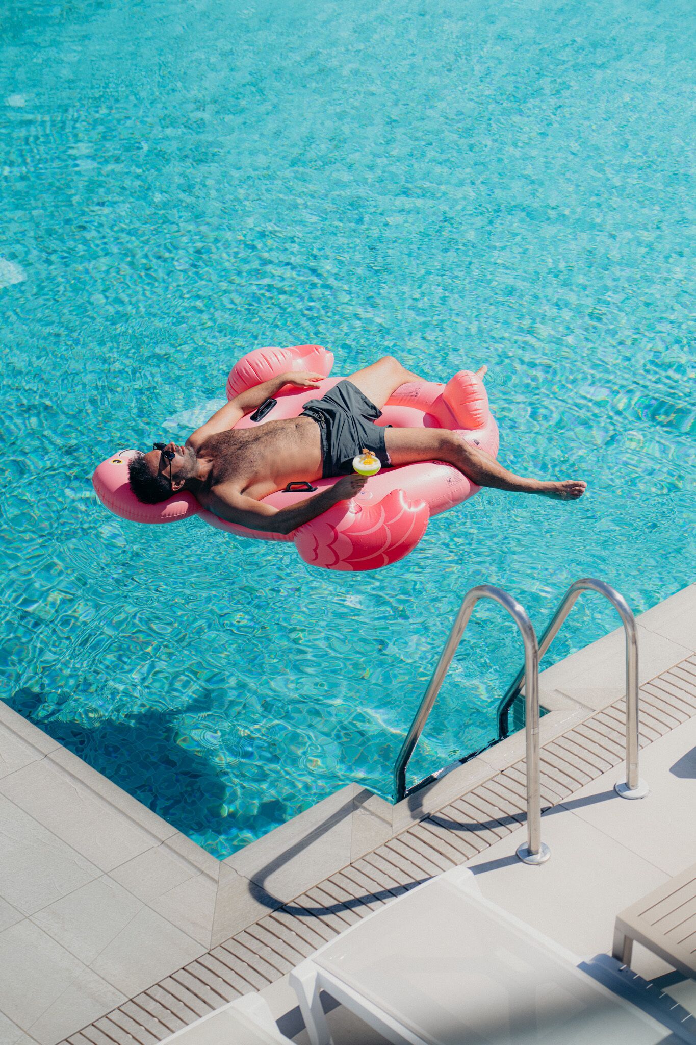 A person floating on a pink inflatable in a clear blue pool.