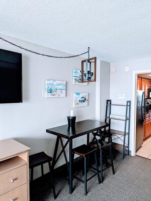 Cozy retreat with a dining table, coffee maker, and TV, surrounded by beach-inspired artwork.