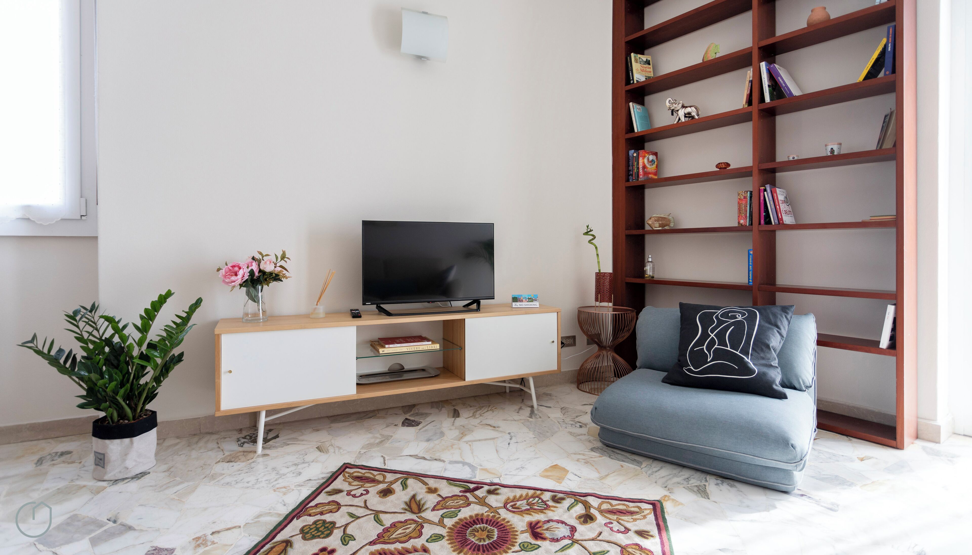 A living room with a TV on a wooden stand, a bookshelf, a sofa, and a potted plant.