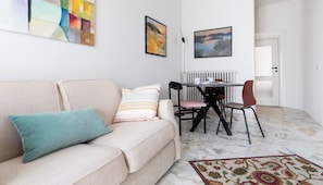 A living room with a sofa, a dining table with chairs, and two paintings on the wall. - Italianway Easy - Sirte 6 (Milan)