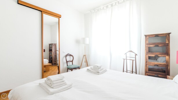 A hotel room with a large bed, a wooden wardrobe, a chair, and a mirror. - Italianway Easy - Montecatini 15 (Milan)