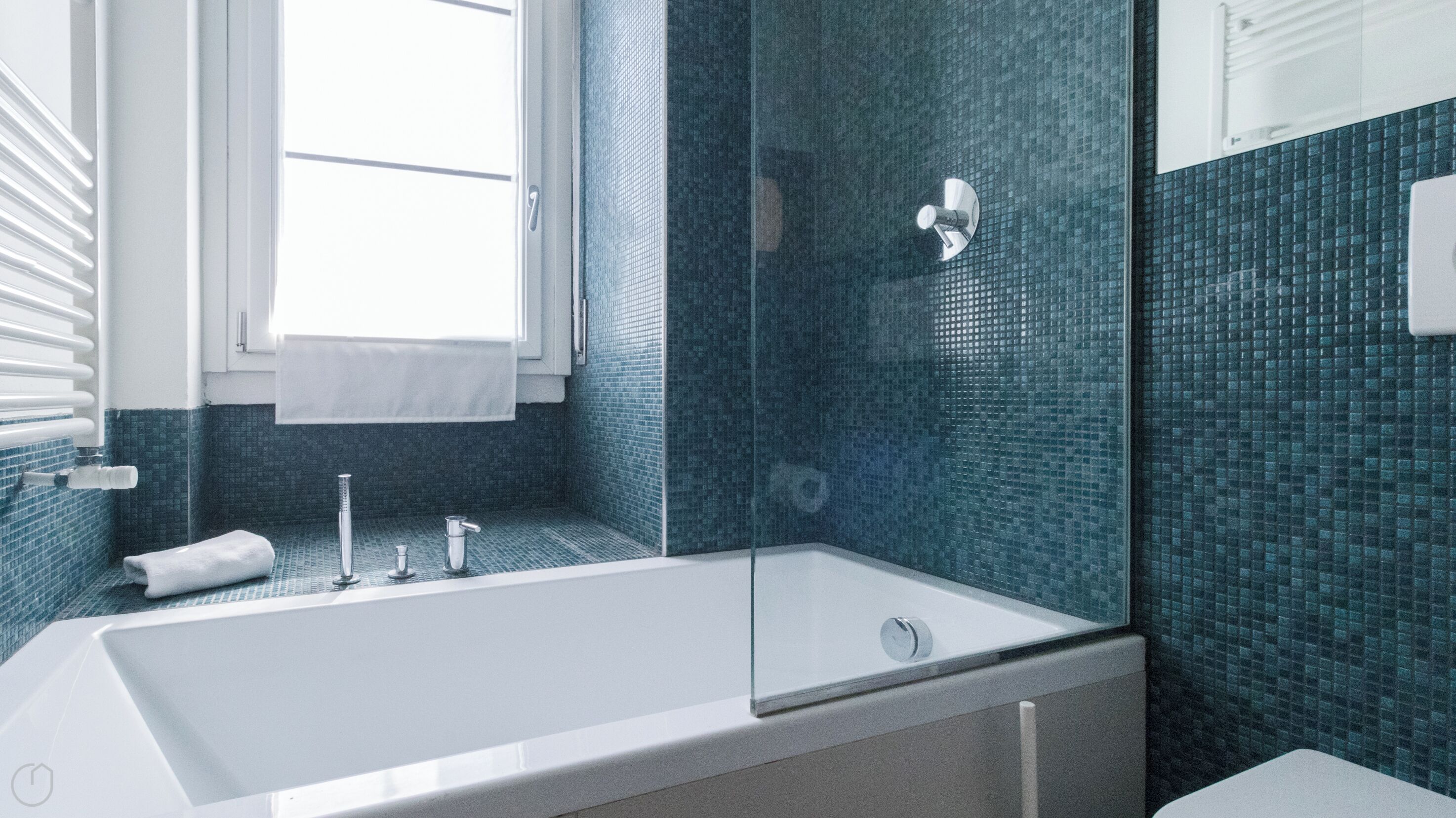 Une salle de bain moderne avec une grande baignoire blanche, une douche en verre et une fenêtre laissant entrer la lumière naturelle.