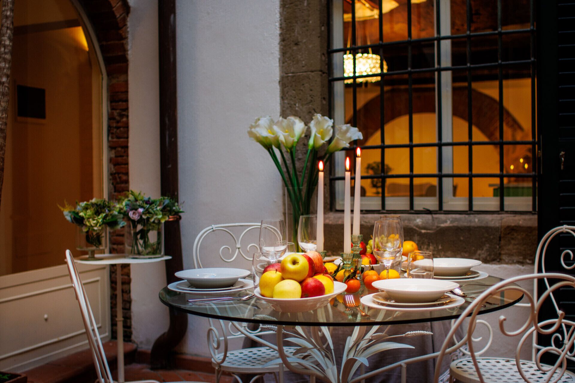 Une table en verre, dressée pour le repas, avec de l’argenterie blanche, des verres et un saladier rempli de fruits.