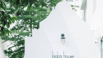 A woman standing in front of a white building with a sign reading "Lada's House" and the number "58" on the wall.