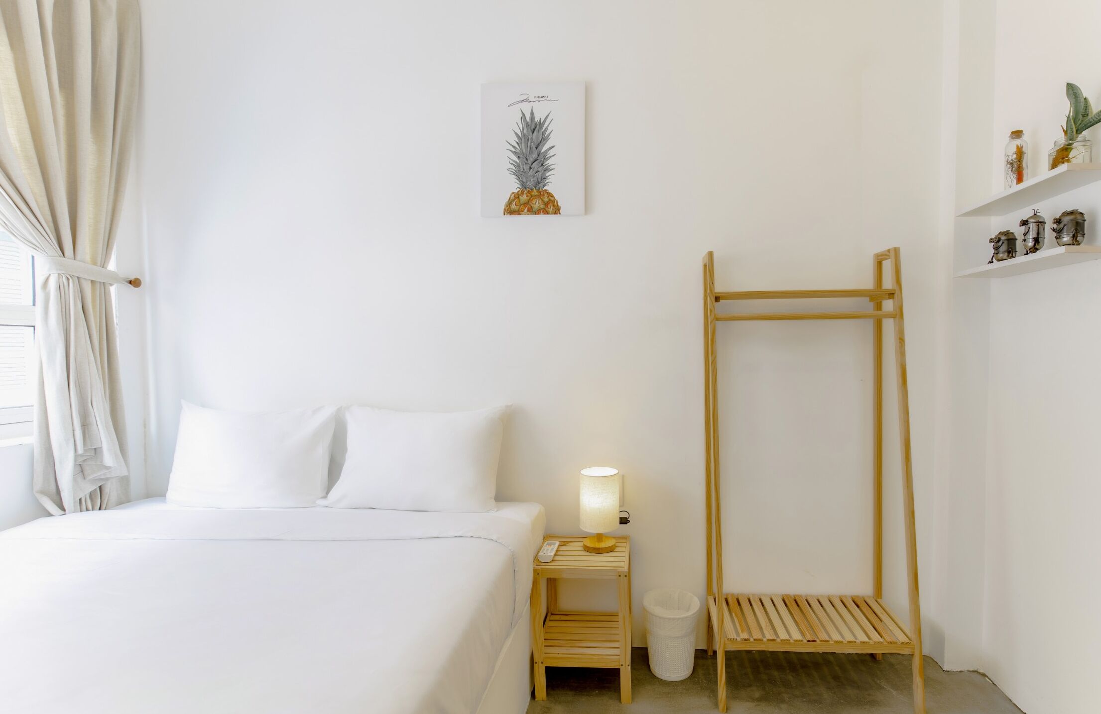 A hotel room with a bed, a nightstand with a lamp, a wooden ladder, a trash bin, and a shelf with decorative items.