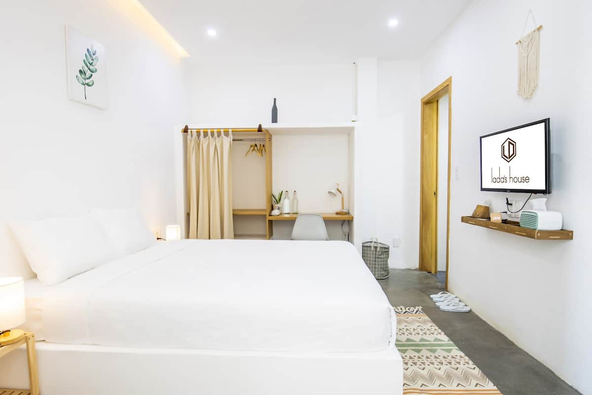 A modern hotel room with a large bed, a desk, a TV, and a wardrobe.