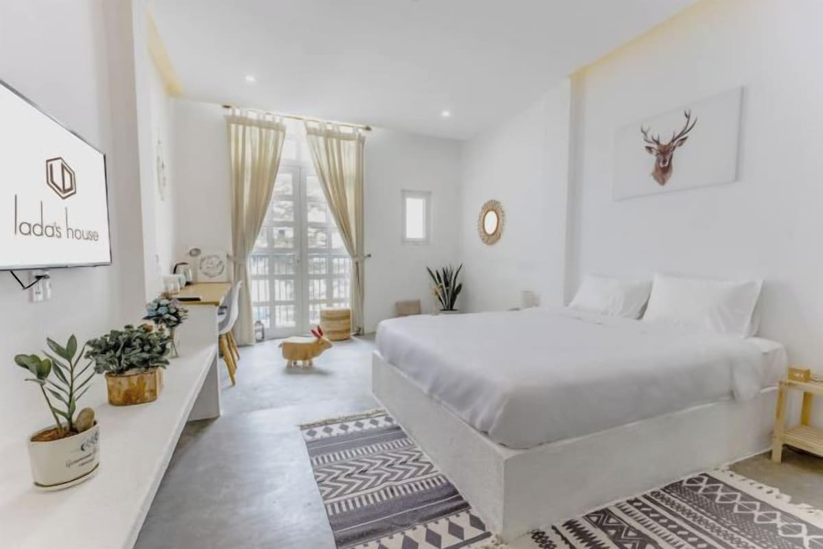 A modern bedroom with a large bed, a bedside table, a mirror, and a wall-mounted TV.