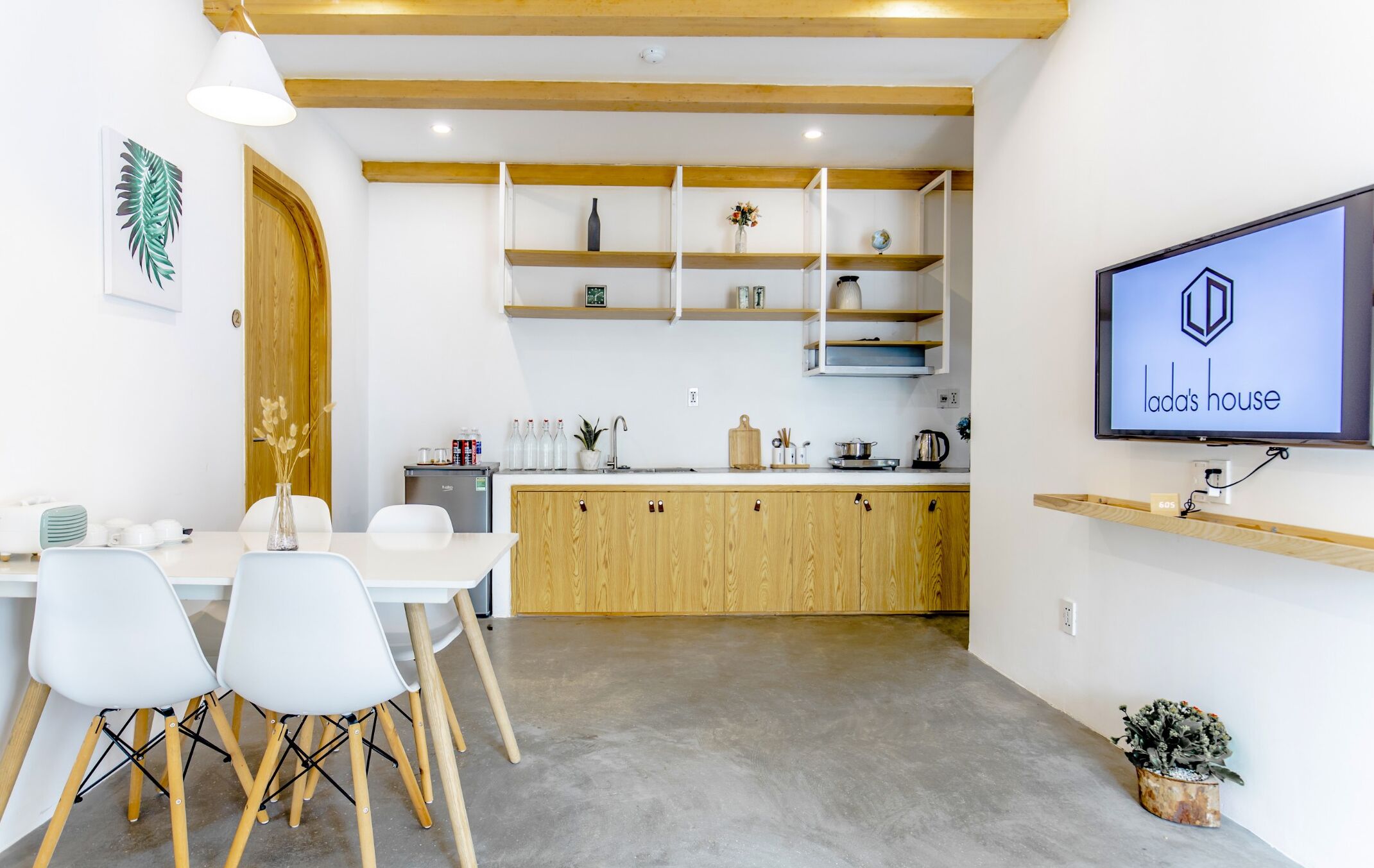 A modern kitchen with wooden cabinets, a dining table with chairs, and a TV displaying 'lada's house'.