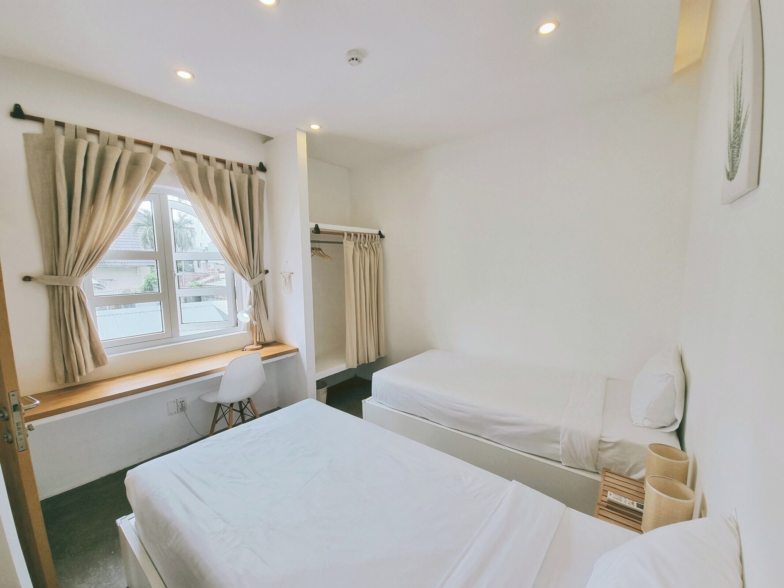 A hotel room with two beds, a desk, a chair, a window with curtains, and a small mirror on the wall.