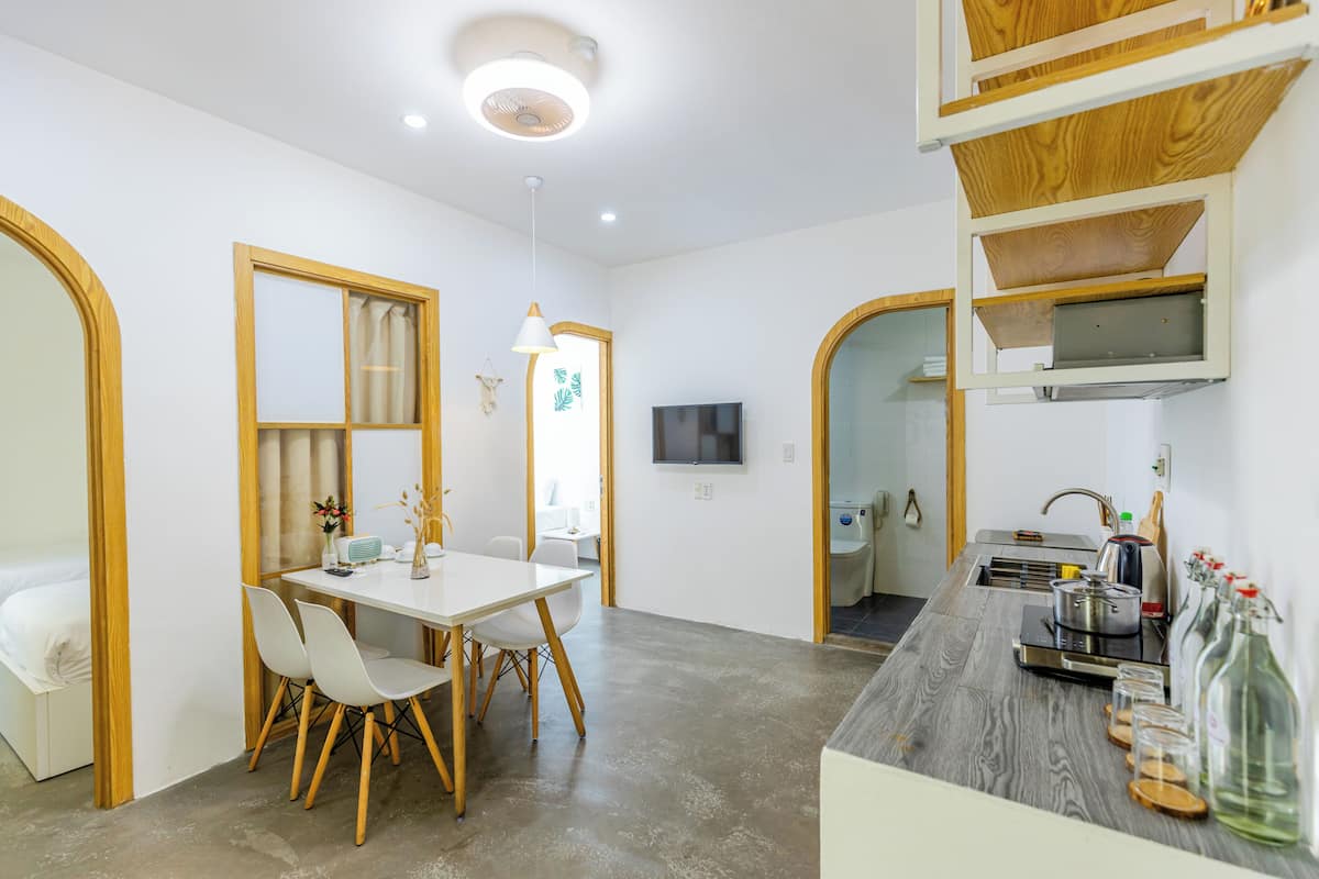 A modern kitchen with a built-in stove, sink, and wooden cabinets. There is a dining area with a white table and chairs.