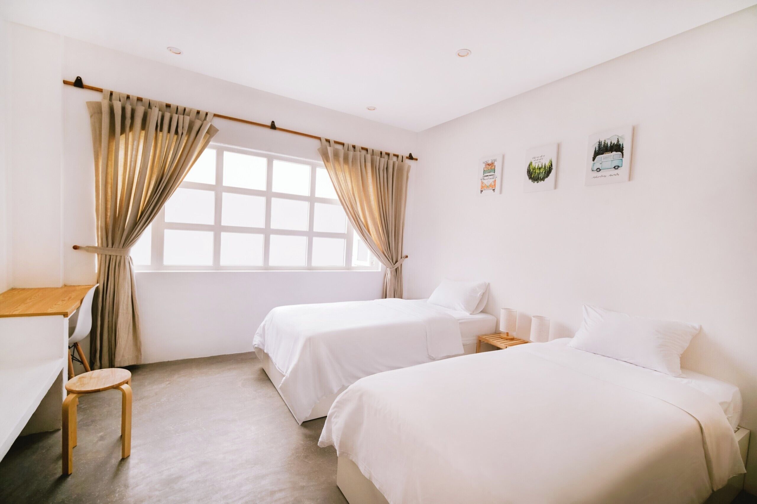 Een hotelkamer met twee eenpersoonsbedden, een bureau met stoel, een tafeltje en een raam met gordijnen.