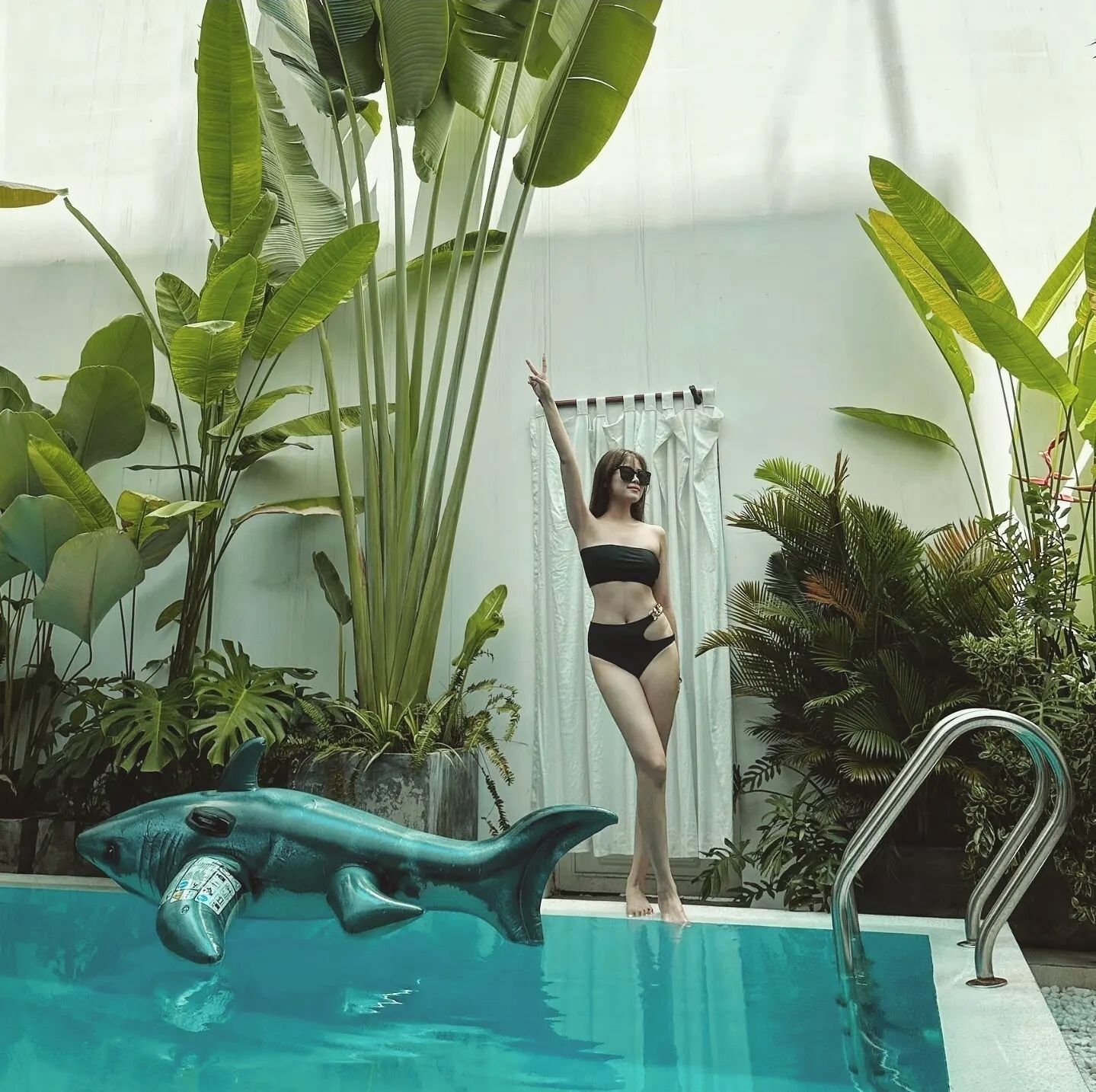 Une femme en maillot de bain noir, debout près d’une piscine, avec une sculpture de dauphin en arrière-plan.