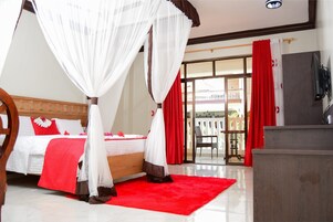 Habitación de hotel con cama, alfombra roja, escritorio de madera y balcón con cortinas rojas.