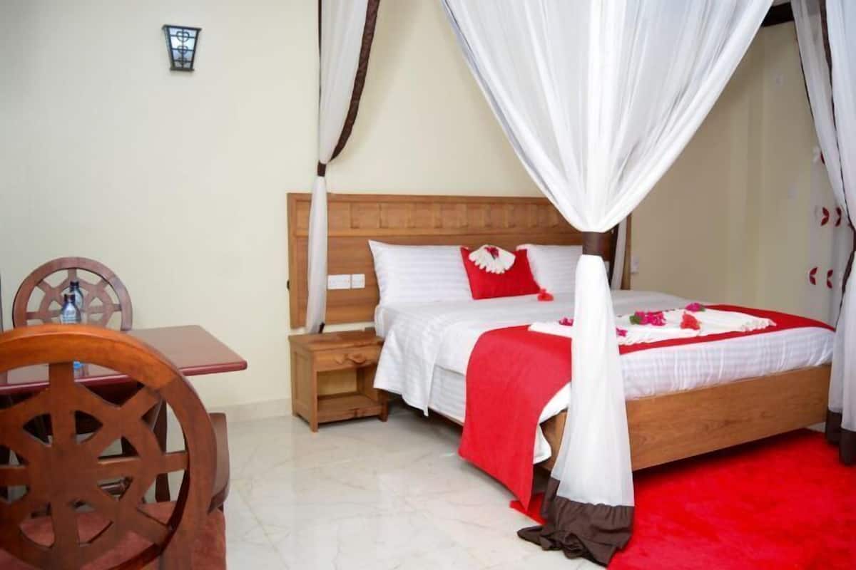 Quarto com cama de madeira, roupa de cama branca, manta vermelha e dossel.