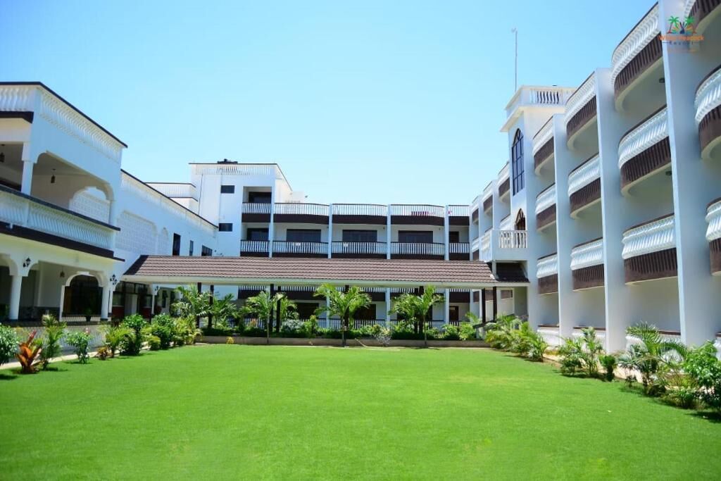 A hotel courtyard with a central lawn, white buildings with balconies, and tropical landscaping.