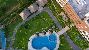 An aerial view of a resort with a large central pool, surrounded by pathways, palm trees, and a building with a unique architectural design. - White Peacock Resort Mtwapa (Mtwapa)