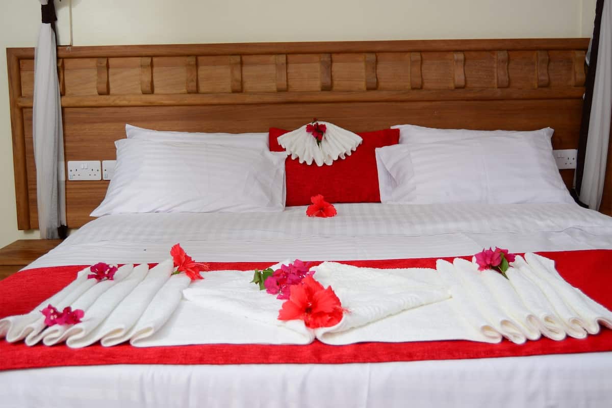 Cama bem arrumada com lençóis brancos, almofadas vermelhas e detalhes florais.