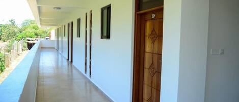 A corridor with a wooden door marked 221, white walls, and a blue railing.
