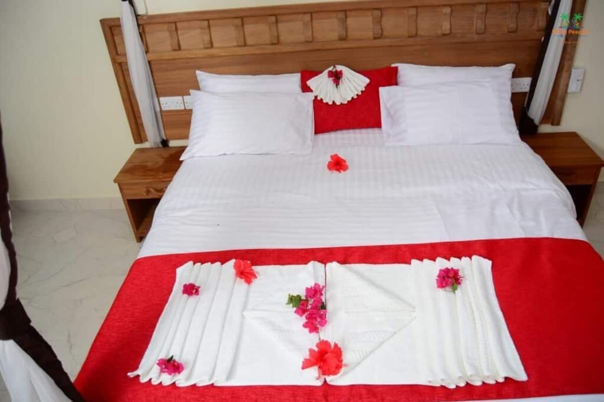 Cama bem arrumada com lençóis brancos, detalhes vermelhos e decorações florais.