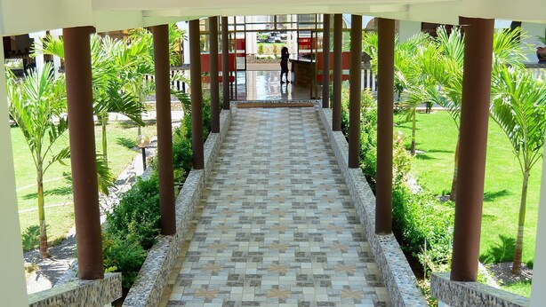 A covered walkway with patterned tiles, surrounded by greenery and palm trees. - White Peacock Resort Mtwapa (Mtwapa)