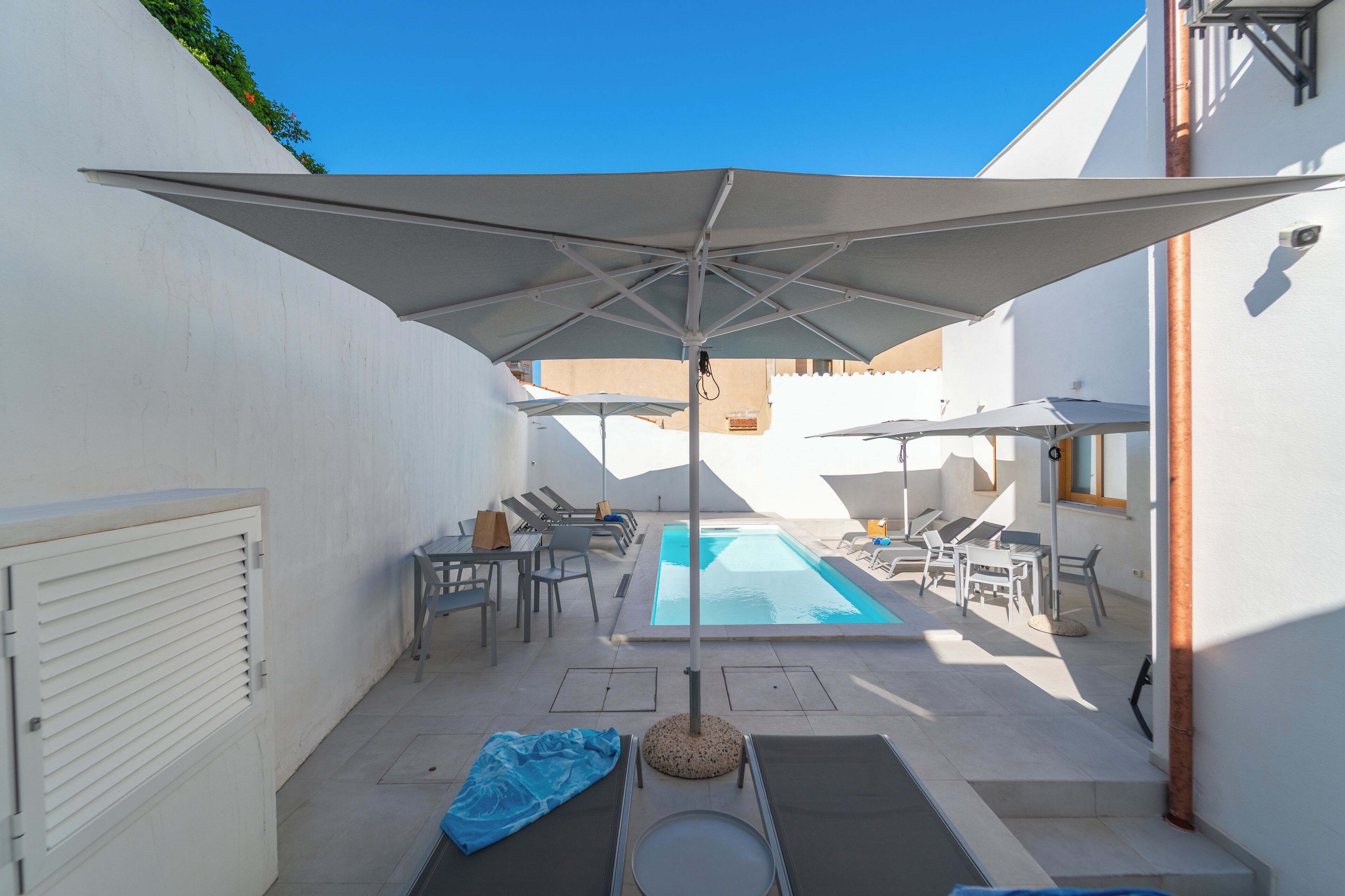Zona de piscina con sillas de descanso, sombrillas y una pileta.